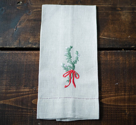 Folded white linen tea towels with hand embroidered floral designs and a bow motif, displayed on a wooden surface.